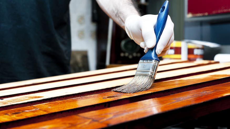 Finish being applied to slats of wood with a brush.