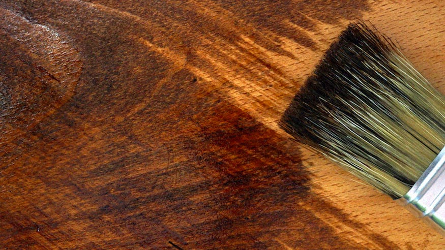 A detail of a brush applying finish to a piece of wood.