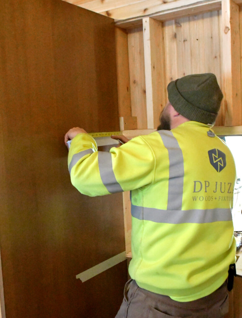 A man uses a tape measure to correctly install the next piece of a closet in the entryway of a house.