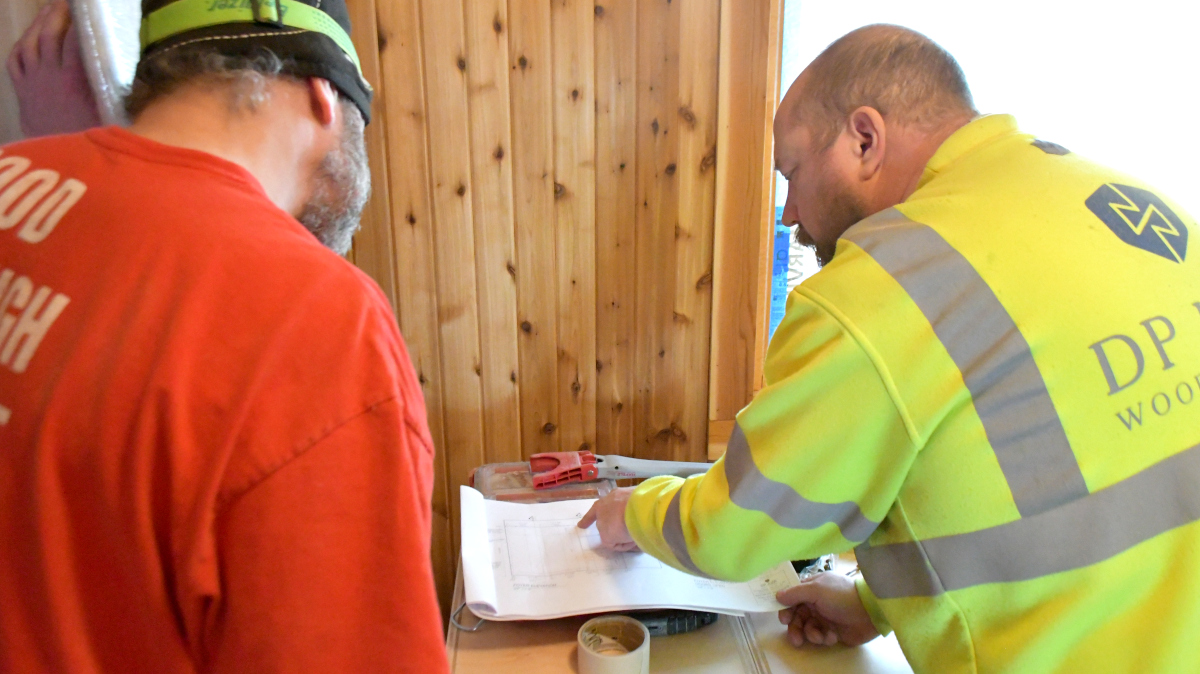 Two men reference job prints while working to install a closet in the entryway of home.