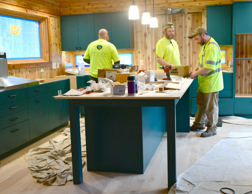 The men work to install various parts of a custom cabinets in a kitchen.