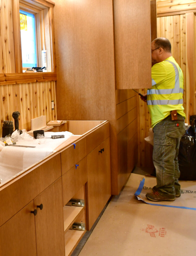 A man works in front of a tall cabinet to install interior features of the cabinet.