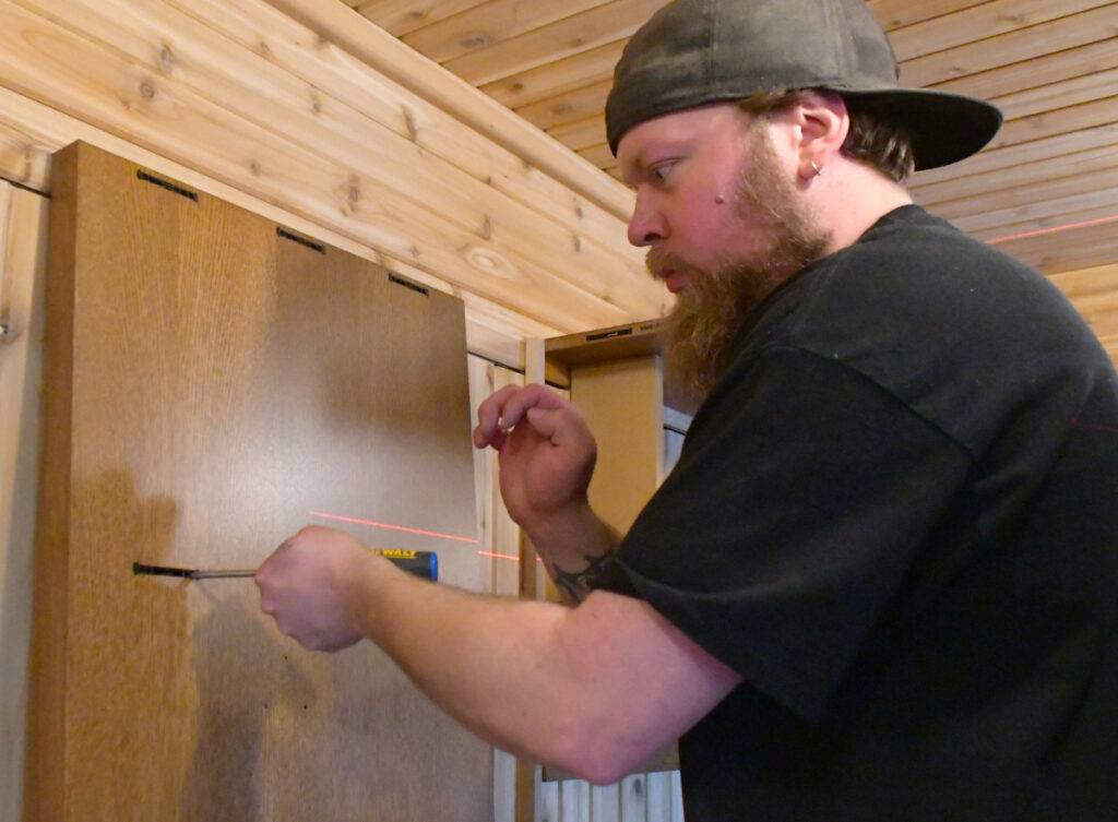 A man uses a screw driver to insert a clip into the side piece of a closet that will attach it to the rest of the closet.