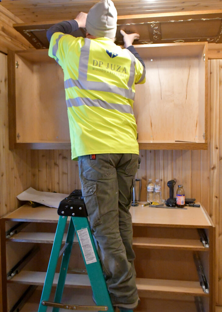 The top of a cabinet is installed by a man standing on a ladder.